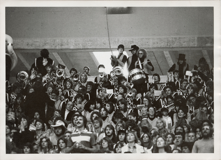 Black and white photograph of a marching band and spectators sitting or standing in stadium bleachers.