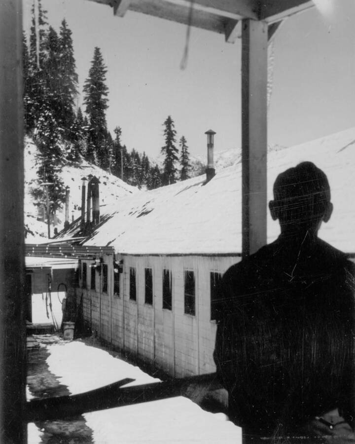 Silhouette of a man looking out at the buildings at Kooskia Internment Camp in winter. Photo taken from 12-3/4 x 15-1/4 Photograph album of the Kooskia Japanese Internment Camp.