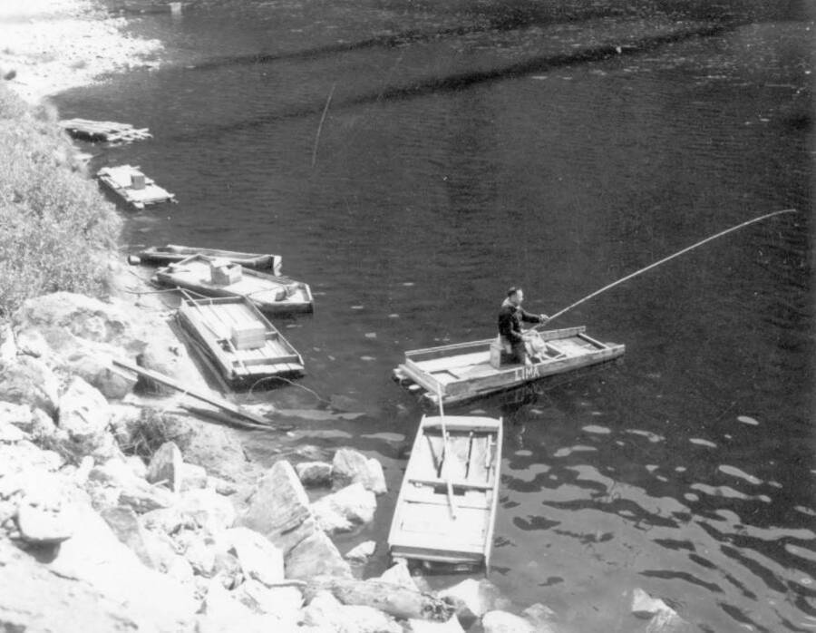 Image of a man at Kooskia Internment Camp fishing in a raft on the Lochsa Lochsa River. Photo taken from 12-3/4 x 15-1/4 Photograph album of the Kooskia Japanese Internment Camp.