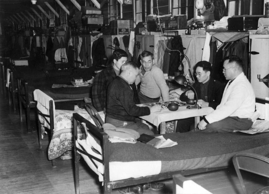 Interior shot of a group of men at Kooskia Internment Camp playing a game while sitting on cots in sleeping quarters. Photo taken from 12-3/4 x 15-1/4 Photograph album of the Kooskia Japanese Internment Camp.