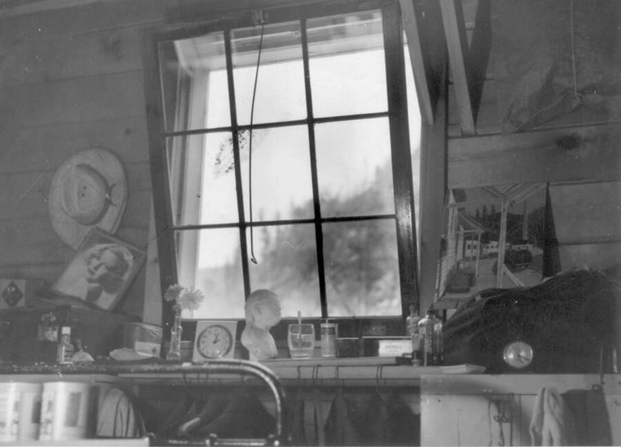 Interior shot of assorted items on windowsill (i.e. pictures, hat, bottles, toothbrush and drinking glass, etc.) in front of an open window at Kooskia Internment Camp. Photo taken from 12-3/4 x 15-1/4 Photograph album of the Kooskia Japanese Internment Camp.