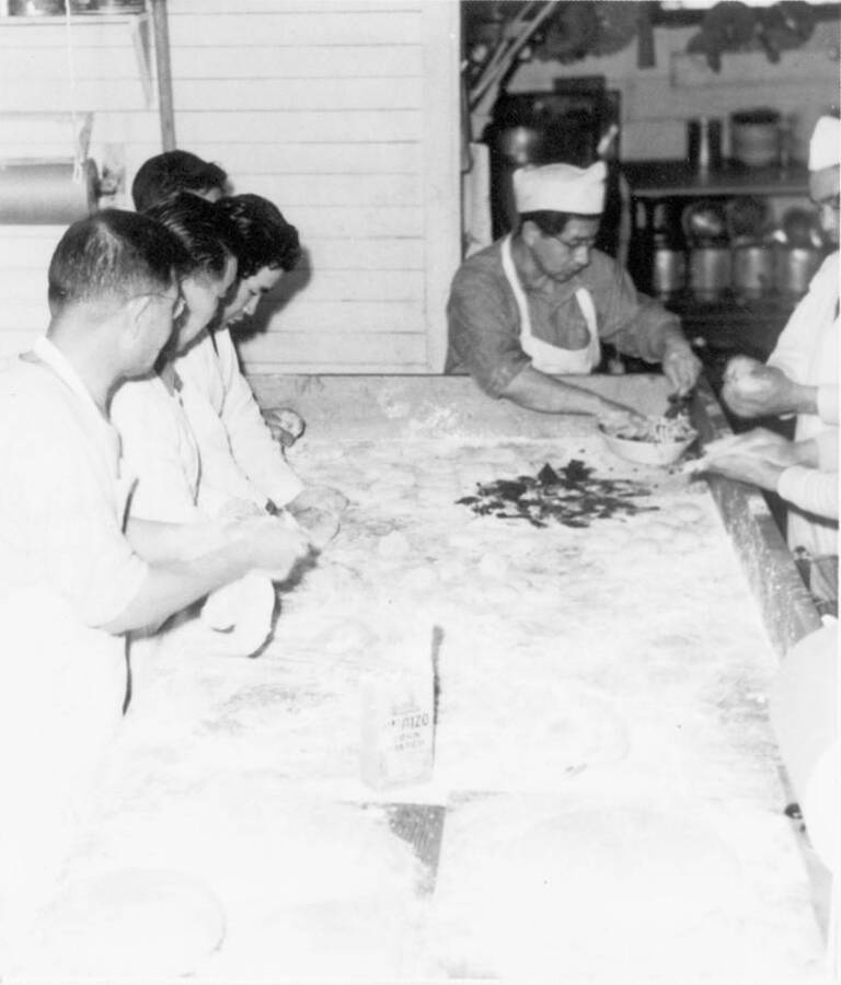 Image of group of men working with flour during food preparation at Kooskia Internment Camp. Photo taken from 12-3/4 x 15-1/4 Photograph album of the Kooskia Japanese Internment Camp.