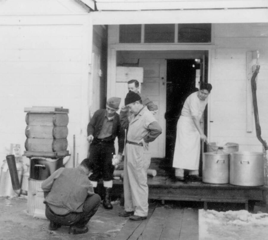 Image of a group of men working on a seiro outside a building at Kooskia Internment Camp. The seiro was used to cook glutinous rice in preparation of making mochi for the New Year's celebration. Photo taken from 12-3/4 x 15-1/4 Photograph album of the Kooskia Japanese Internment Camp.