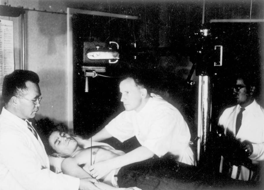 Interior view of men in medical uniform attending to a patient at Kooskia Internment Camp.. Photo taken from 12-3/4 x 15-1/4 Photograph album of the Kooskia Japanese Internment Camp.