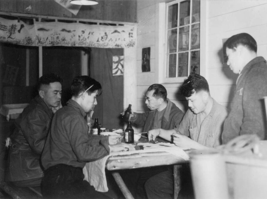 Interior image of a group of men sitting at a table playing a card game at Kooskia Internment Camp. Photo taken from 12-3/4 x 15-1/4 Photograph album of the Kooskia Japanese Internment Camp.