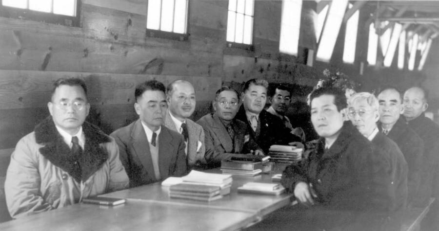 Interior shot of group of men sitting at table for a meeting at Kooskia Internment Camp. Photo taken from 12-3/4 x 15-1/4 Photograph album of the Kooskia Japanese Internment Camp.
