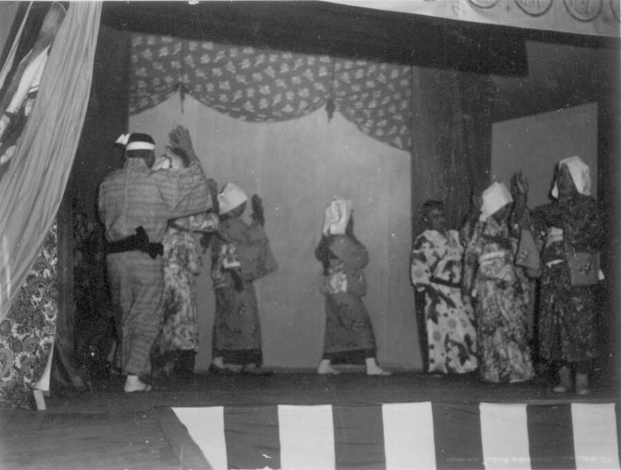 Interior shot of a staged performance with men wearing traditional costumes at Kooskia Internment Camp. Photo taken from 12-3/4 x 15-1/4 Photograph album of the Kooskia Japanese Internment Camp.