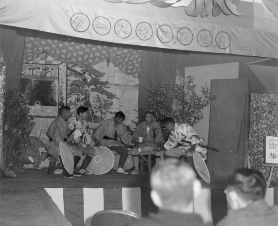 Interior shot of a group of men sitting on stage during a performance in traditional costume  at Kooskia Internment Camp. Photo taken from 12-3/4 x 15-1/4 Photograph album of the Kooskia Japanese Internment Camp.