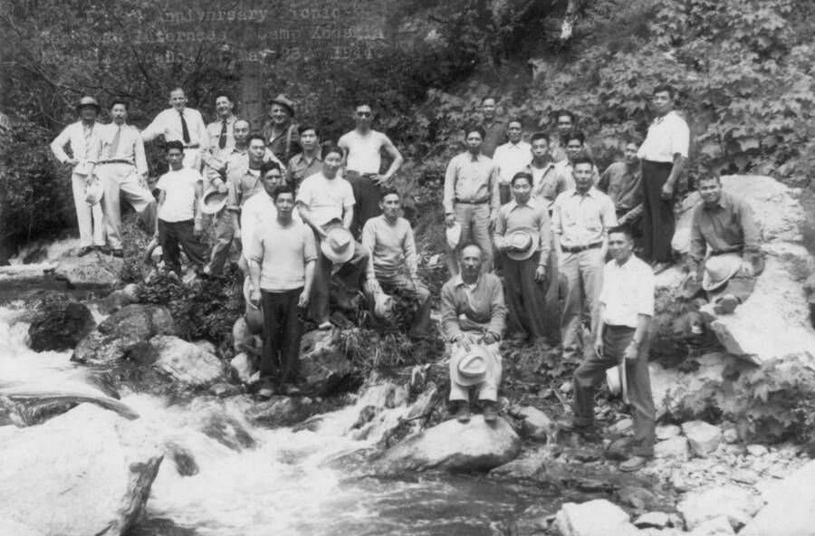 Image of large group of men by a stream; type on photo reads, " Anniversary Japanese Internees, Camp Kooskia, Kooskia Idaho, May 28, 1944." Photo taken from 12-3/4 x 15-1/4 Photograph album of the Kooskia Japanese Internment Camp.