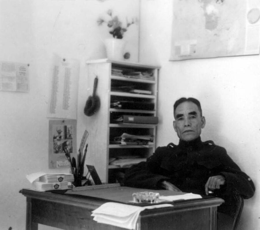 Interior shot of man sitting at desk at Kooskia Internment Camp. Photo taken from 12-3/4 x 15-1/4 Photograph album of the Kooskia Japanese Internment Camp.