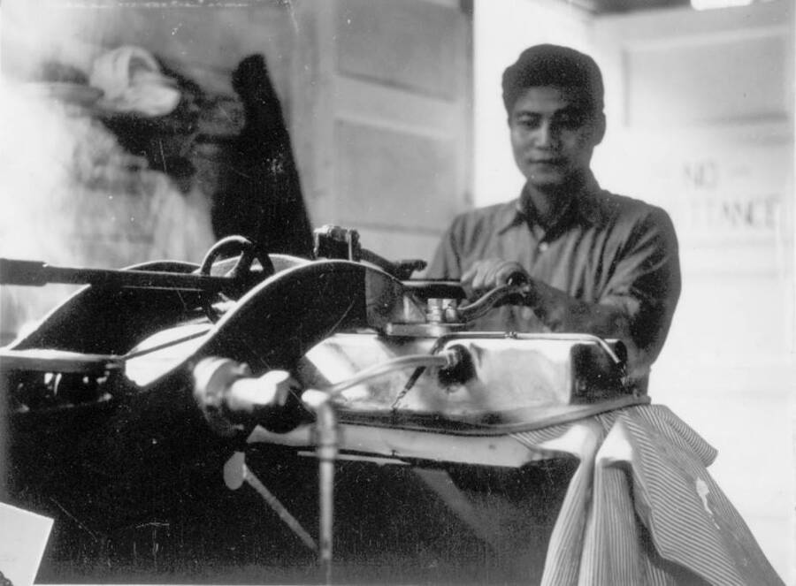 Interior shot of man pressing clothes at Kooskia Internment Camp. Photo taken from 12-3/4 x 15-1/4 Photograph album of the Kooskia Japanese Internment Camp.