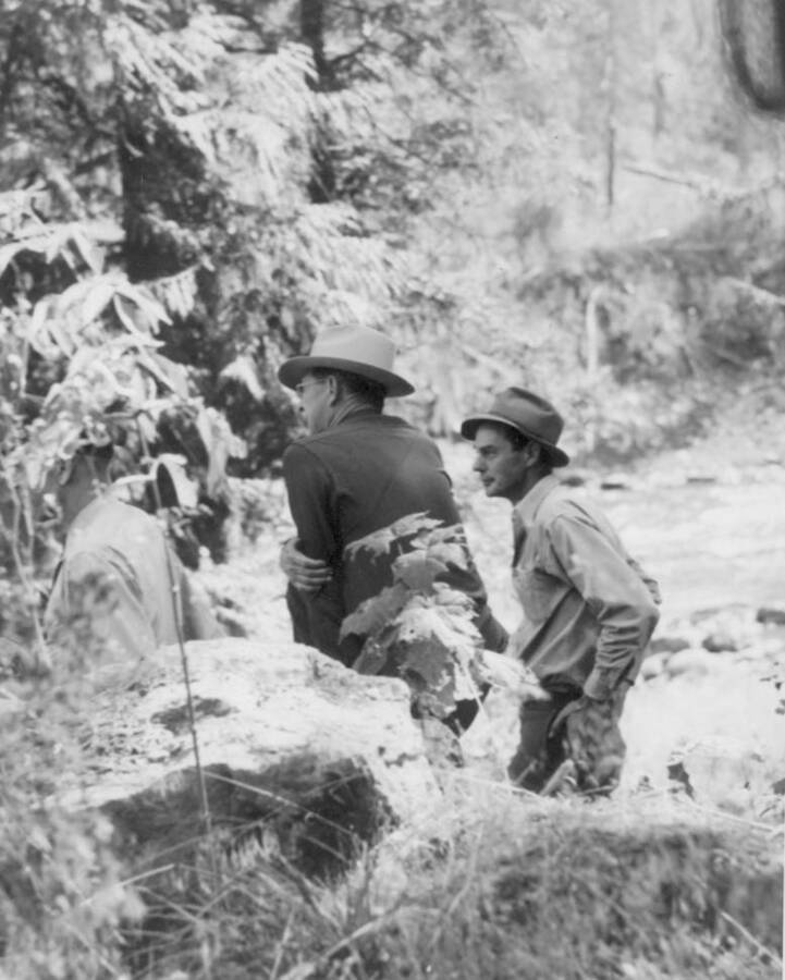 Image of three men by  the Lochsa Lochsa River at Kooskia Internment Camp as they oversee a construction team. Photo taken from 12-3/4 x 15-1/4 Photograph album of the Kooskia Japanese Internment Camp.