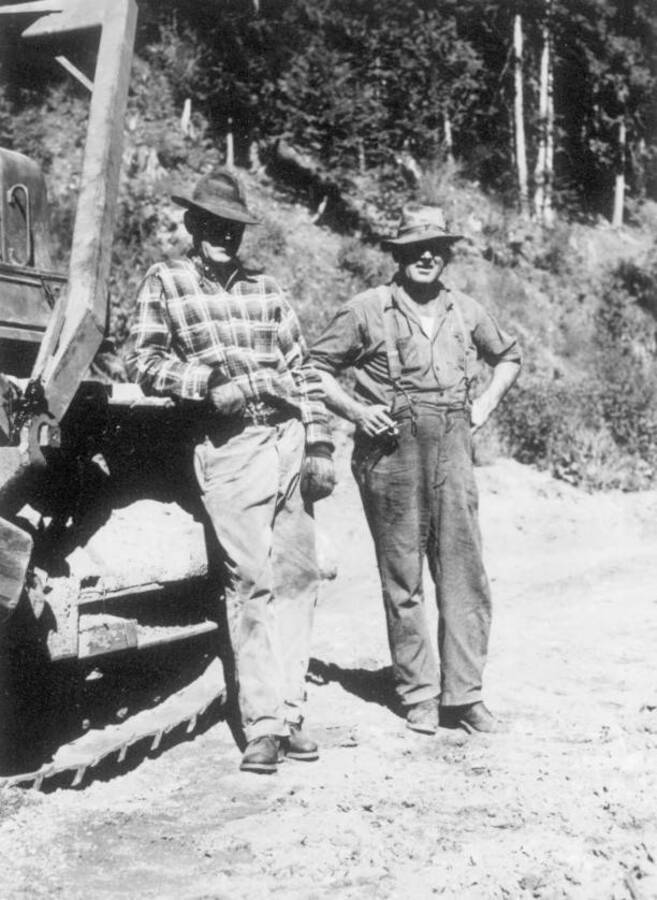 Image of two men standing beside and leaning on construction equipment at Kooskia Internment Camp. Photo taken from 12-3/4 x 15-1/4 Photograph album of the Kooskia Japanese Internment Camp.