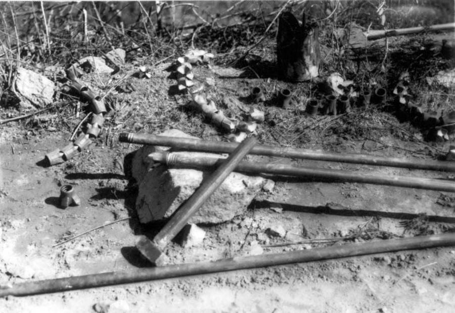 Image of  metal pipes laying on the ground  at Kooskia Internment Camp. Photo taken from 12-3/4 x 15-1/4 Photograph album of the Kooskia Japanese Internment Camp.