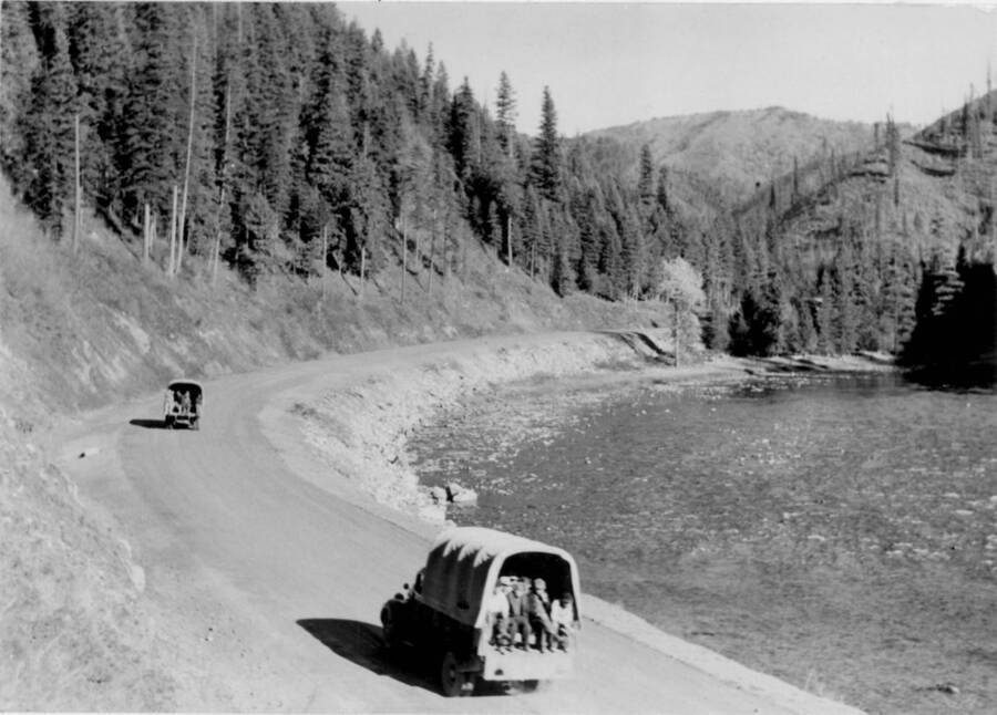 Image of people being transported in vehicles on road beside the Lochsa River near the Kooskia Internment Camp. Photo taken from 12-3/4 x 15-1/4 Photograph album of the Kooskia Japanese Internment Camp.