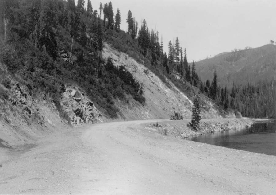 Image of gravel road beside the Lochsa River with a vehicle in the distance at Kooskia Internment Camp. Photo taken from 12-3/4 x 15-1/4 Photograph album of the Kooskia Japanese Internment Camp.
