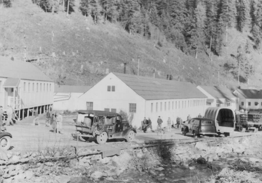 Image of people, vehicles and buildings at Kooskia Internment Camp.. Photo taken from 12-3/4 x 15-1/4 Photograph album of the Kooskia Japanese Internment Camp.