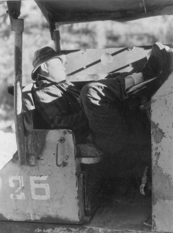 Image of man napping in the seat of a piece of construction equipment at Kooskia Internment Camp. Photo taken from 12-3/4 x 15-1/4 Photograph album of the Kooskia Japanese Internment Camp.