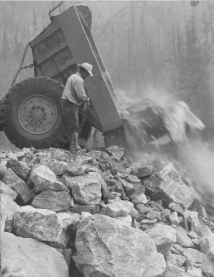 Image of man in front of a dump truck dumping rocks and debris near Kooskia Internment Camp. Photo taken from 12-3/4 x 15-1/4 Photograph album of the Kooskia Japanese Internment Camp.