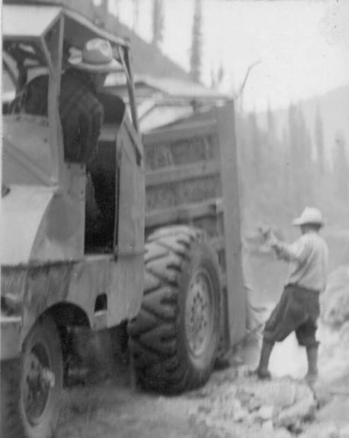 Image of two men moving rocks with construction equipment in front of Lochsa River at Kooskia Internment Camp. Photo taken from 12-3/4 x 15-1/4 Photograph album of the Kooskia Japanese Internment Camp.