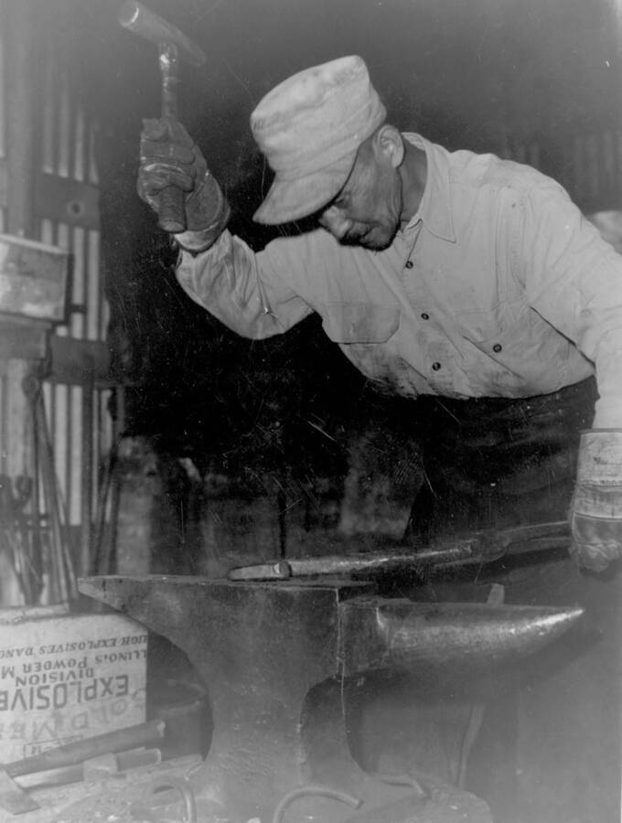 Interior image of Kooskia Internment Camp man working with hammer and anvil. Photo taken from 12-3/4 x 15-1/4 Photograph album of the Kooskia Japanese Internment Camp.