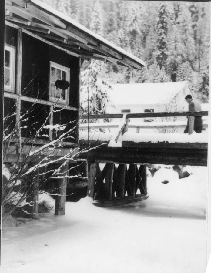 Image of man crossing bridge at Kooskia Internment Camp in winter. Photo taken from 12-3/4 x 15-1/4 Photograph album of the Kooskia Japanese Internment Camp.