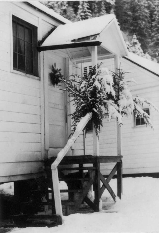 Image of a Kooskia Internment Camp building's porch adorned with boughs of greenery and fir trees. Photo taken from 12-3/4 x 15-1/4 Photograph album of the Kooskia Japanese Internment Camp.