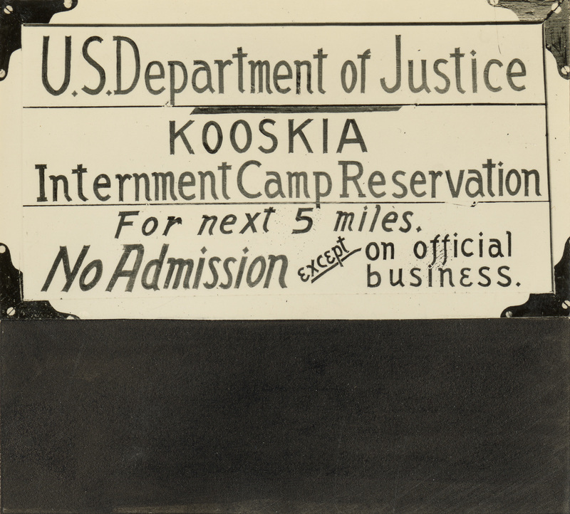 A black and white photo of a sign from the Kooskia Internment Camp. It reads "US Department of Justice. Kooskia. Internment Camp Reservation. For next 5 miles. No Admission except on official business."