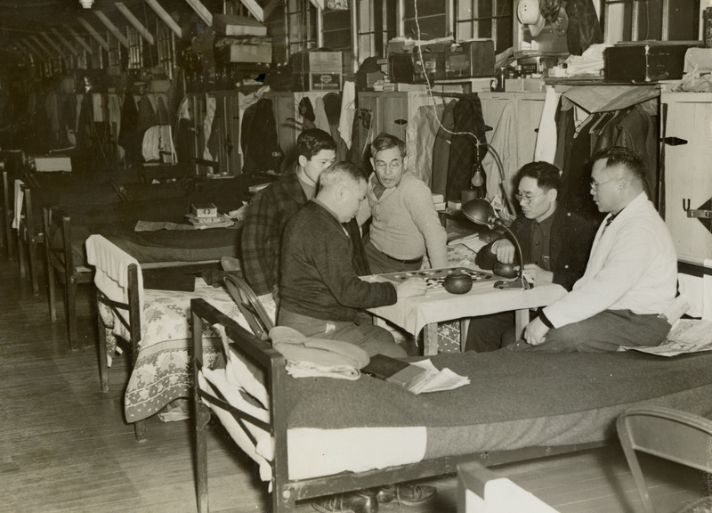 A black and white photograph of men sitting around a table playing games.