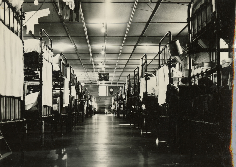 A black and white photograph of the interior of a building at Kooskia. There are rows of bunk beds in a long building.