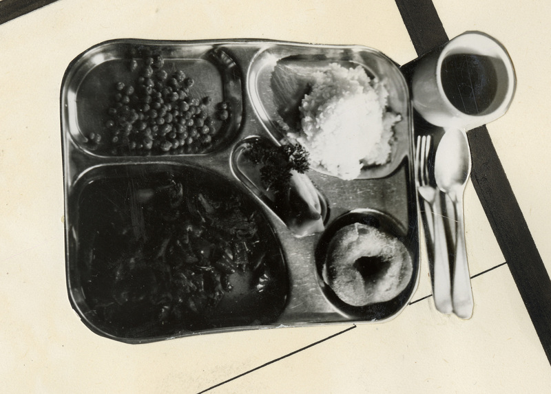 A black and white cutout from a photograph of a meal from Kooskia. Includes food, a drink, silverware, and the tray. 