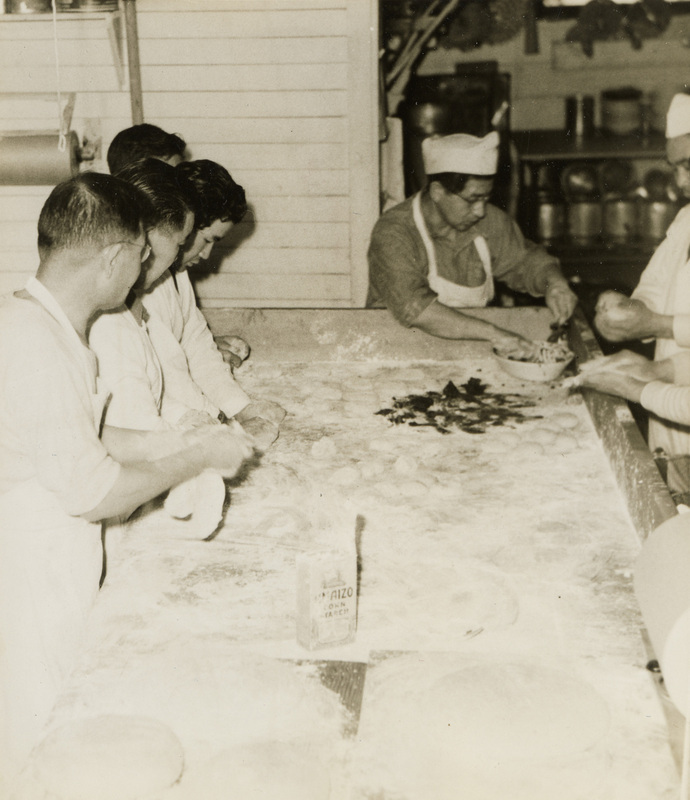 A black and white photograph of men working with flour at a large table.