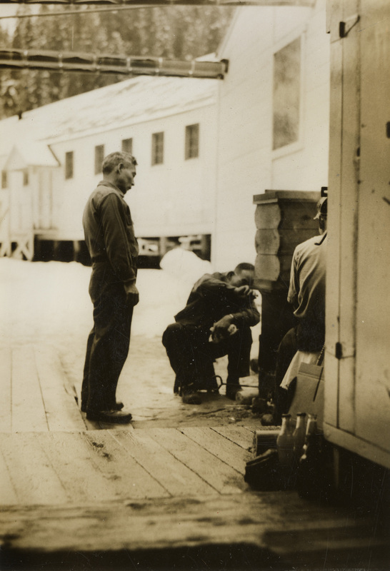 A black and white photograph of three men outside looking at a wood box, called a seiro. 