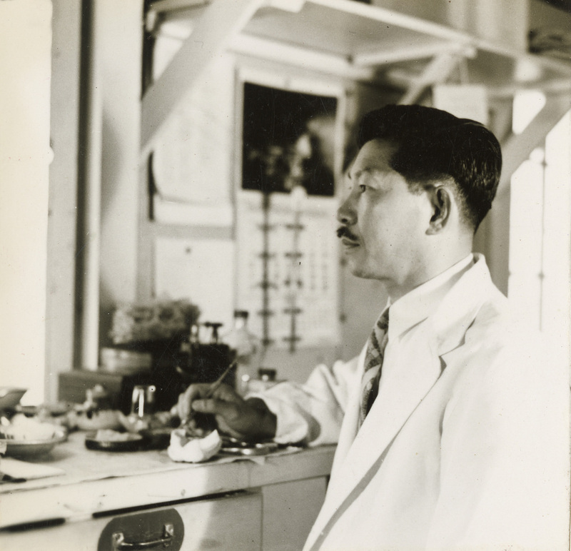 A black and white photograph of a man in a dental jacket. He is holding a tool.