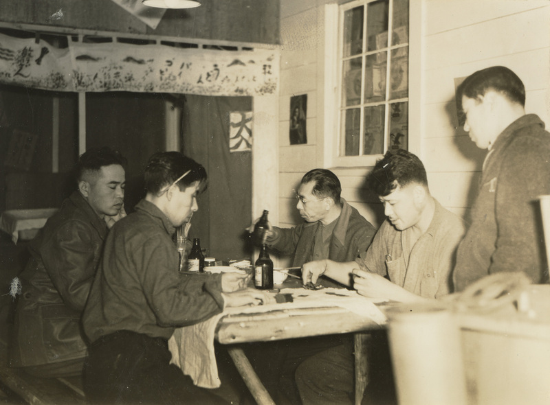 A black and white photograph of five men sitting around a table playing a card game.