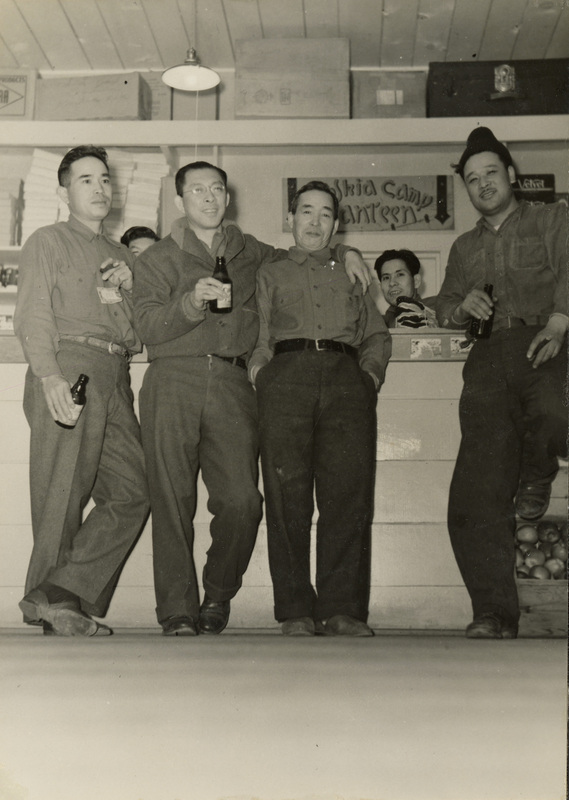 A black and white photograph of a group of men sitting in front of a counter and drinking beverages.