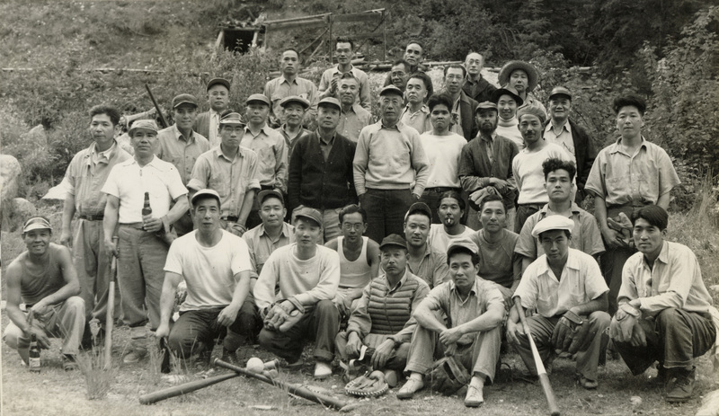 A black and white photograph of a baseball team. Baseball bats are balanced at the front and center of the group.