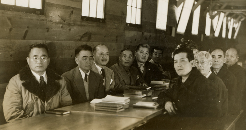 A black and white image of a large group of men sitting at a table, presumably for a meeting. 