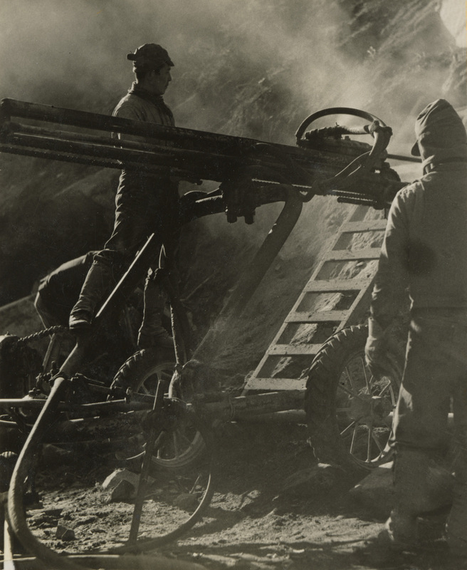 A black and white photograph of three men working with construction equipment.