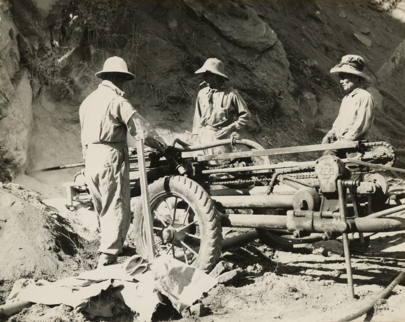 A black and white image of three men standing next to construction and drilling equipment.