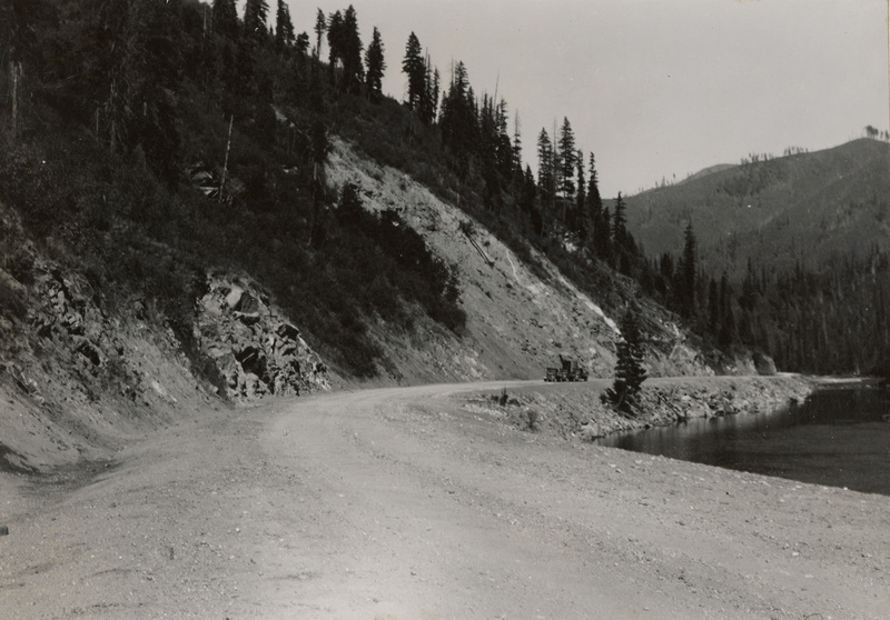 A black and white photograph of a gravel road along a river.