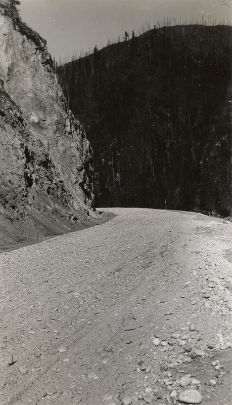 A black and white photograph of a gravel road along a river.