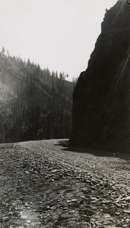A black and white photograph of a gravel road along a river.