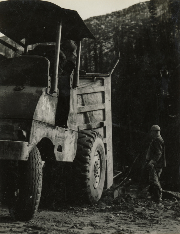 A black and white photograph of two men working with a dump truck.