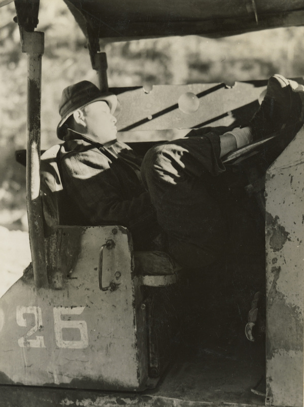 A black and white photograph of a man taking a nap in a truck.