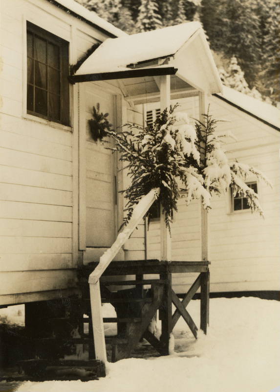 A black and white photograph of a building with greenery wrapped around the porch of a building during winter.