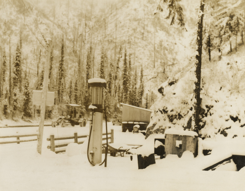 A black and white photograph of miscellaneous equipment in winter. There includes a sign facing the opposite direction of the camera and a few outdoor boxes.
