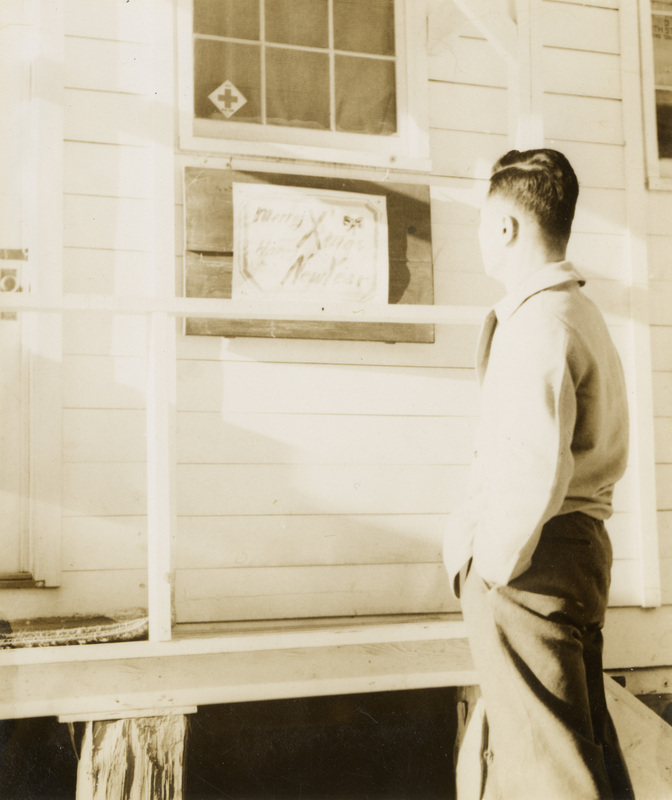 A black and white image of a man looking at a sign in a window of a building. The sign reads "Merry X-mas and Happy New Year". 