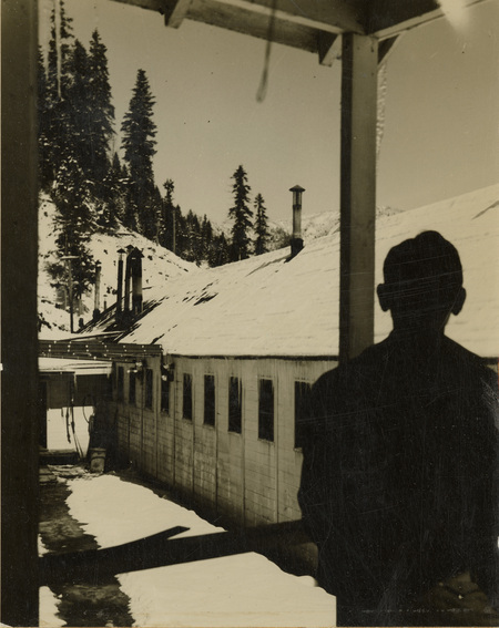 A black and white photo of a silhouette of a man looking at buildings in the foreground.