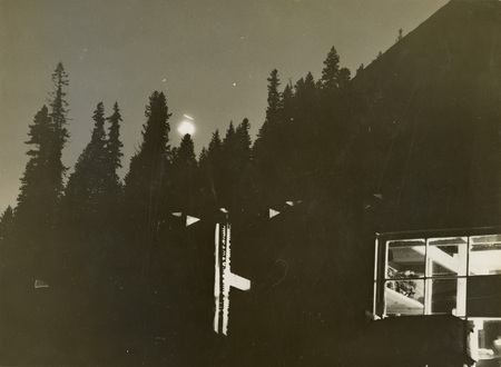 A black and white photograph of the internment camp at night. Lights are shown coming from the windows of a building.
